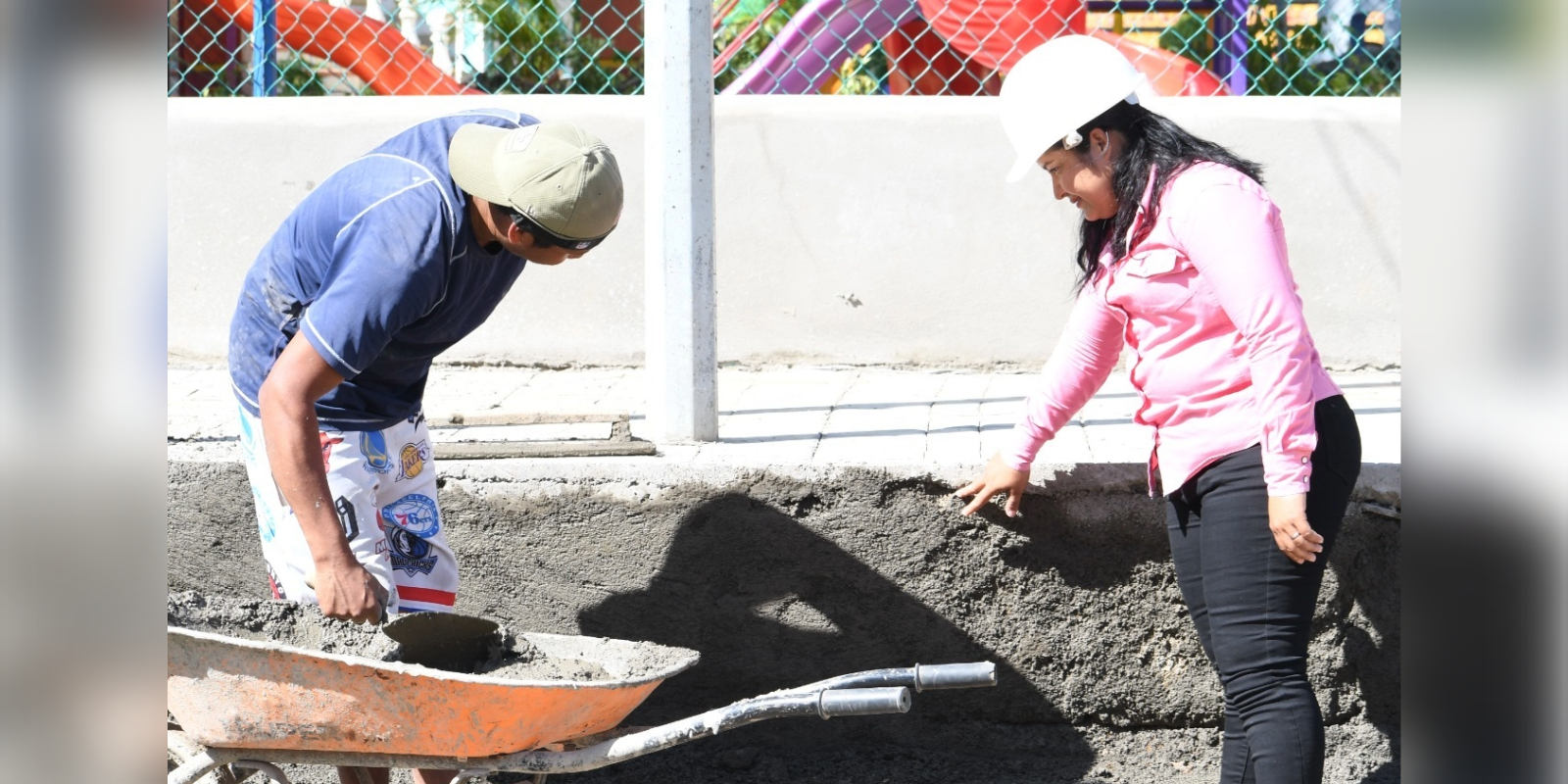 Madeling Benavides señala un área específica en la obra mientras conversa con otro trabajador, mostrando su rol como supervisora en el proyecto de mejoramiento del parque central.